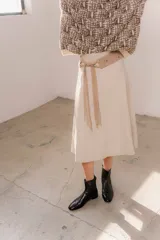 Pollera midi de eco cuero color beige, de corte recto y tiro alto, con costuras verticales decorativas y detalle de cinturón fino con flecos.