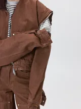 Campera de denim a rayas verticales con cuello de pana en color bordó. Presenta cierre frontal, mangas desmontables con cierre en los hombros, canesú en el pecho y bolsillos de parche cuadrados.