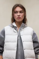 Chaleco acolchado blanco sin mangas, con diseño de franjas horizontales, cuello alto y cierre frontal con botones a presión. Modelo Olimpo de Ecoalf.