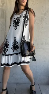 Vestido corto blanco con estampado de flores negras, corte suelto y ruedo con volantes.