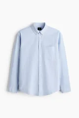 Camisa de algodón Oxford con cuello americano, bolsillo frontal y mangas largas con puños abotonados. Presenta un corte estándar y bajo redondeado.