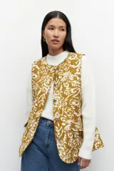 Chaleco capitoneado color crema con estampado floral en tonos marrones. Cuenta con cuello mao, cierre frontal con botones grandes y lazo en la misma tela para acentuar la cintura.