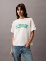 Remera de algodón color blanco hueso, corte boxy, con mangas cortas con dobladillo y logo de Calvin Klein estampado en verde. Diseño de estilo universitario.
