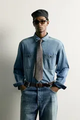 Camisa relaxed fit confeccionada en denim ligero de algodón, con cuello solapa, manga larga con puño abotonado, dos bolsillos de parche en el pecho con solapa y cierre frontal de botones. Presenta un efecto de lavado desgastado.