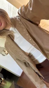 Campera corta de ecocuero color beige, con diseño de solapas y cierre frontal con botones a presión metálicos.