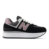 Championes urbanos New Balance modelo 574 con plataforma, confeccionados en una combinación de gamuza y malla. Presentan un diseño en color negro con detalles en lila y blanco, destacando el logo 'N' característico en los laterales.