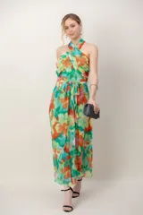 Vestido largo de gasa estampado con diseño floral en tonos verdes, naranjas y amarillos. Cuenta con escote halter cruzado, tiras para atar en la cintura y falda fluida al tobillo.