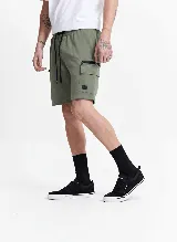 Short cargo de felpa sin frisa, color verde militar, con cintura elástica ajustable mediante cordones. Presenta bolsillos laterales tipo cargo con cierre y solapa, y un pequeño parche decorativo en el bolsillo izquierdo.