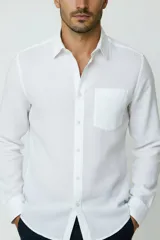 Camisa blanca de manga larga, con cuello camisero, cierre frontal de botones y un bolsillo aplicado en el pecho.