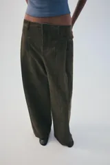 Pantalón verde militar de tiro medio, con bolsillos delanteros, pliegues y tejido con efecto lavado. Cuenta con cierre frontal con cremallera y gancho metálico.
