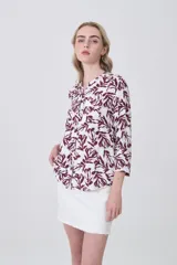 Camisa de viscosa con estampado botánico en tonos bordó sobre fondo blanco, cuello mao y cierre frontal con botones. Presenta bolsillos frontales y mangas tres cuartos.