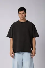 Remeron de corte oversized con cuello redondo y mangas cortas. Presenta un acabado de tela con efecto desgastado y costuras visibles en los bordes, con una etiqueta pequeña en el lateral inferior.