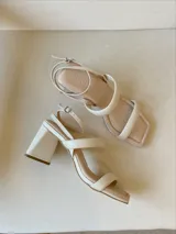 Sandalias de tacón color beige con tiras finas y hebilla en el tobillo.