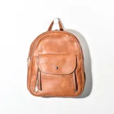 Mochila pequeña color marrón de cuero sintético, con bolsillo frontal con cierre a presión y dos bolsillos laterales con cierre.