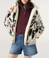 Campera bomber reversible con un lado de corderito estampado con manchas abstractas en tonos negro, marrón, azul y violeta sobre fondo blanco, y del otro lado liso en tono crudo.