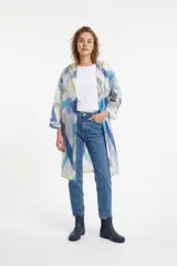 Piloto impermeable de corte recto y largo midi, confeccionado en material translúcido con estampado abstracto en tonos azules, grises y amarillos. Cuenta con capucha, cierre frontal mediante botones a presión y mangas tres cuartos.