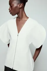 Top de Zara Woman Collection color blanco, con escote en pico, mangas cortas abullonadas con aberturas y cierre frontal con cremallera.