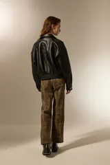 Campera de eco-cuero color negro, con cuello clásico, cierre frontal y puños con elástico. Presenta un diseño de corte holgado con costuras verticales decorativas.