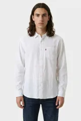 Camisa de manga larga confeccionada en lino, color blanco, con cuello clásico, cierre frontal de botones y un bolsillo en el pecho con etiqueta roja distintiva.
