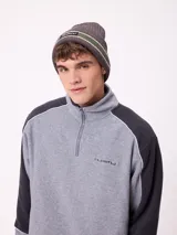 Gorro tipo beanie de punto en color gris, con franjas horizontales en verde y blanco, y logo de la marca Rusty en el frente.