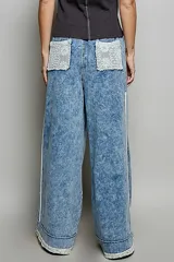 Pantalon de denim azul con lavado vintage, corte ancho y recto, cintura elastizada, grandes bolsillos delanteros de encaje y detalles de ribetes trenzados.