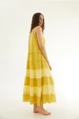 Vestido largo de lino color amarillo mostaza, sin mangas con diseño de espalda nadadora y escote a la base, con detalles de mini volados horizontales escalonados a lo largo de la falda.