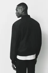 Campera bomber negra, de corte estándar, con cuello elevado acanalado, cierre frontal y bolsillos laterales con cierre. Presenta puños y bajo con ribete acanalado ancho.