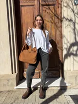 Cartera tipo tote bag de cuero color camel, con detalles de tachas metálicas en el bolsillo frontal y tiras largas para el hombro.
