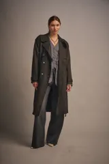 Trench largo color marrón oscuro de gamuza, con solapas amplias, charreteras en los puños y cinturón de la misma tela para ajustar en la cintura. Sin forro.