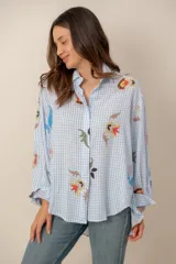 Camisa de corte oversize, con estampa a cuadros vichy en celeste y blanco, complementada con llamativos motivos florales bordados y de manga larga.