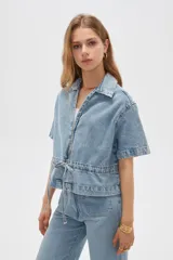 Blusa de jean de manga corta, corte holgado, con cuello en V, cierre frontal con botones y detalles de frunces.