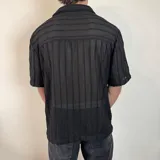 Camisa de manga corta confeccionada en tejido de crochet con diseño de rayas verticales, cuello solapa y cierre frontal con botones.