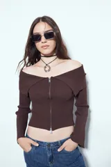Top de punto acanalado negro, con diseño off-shoulder y escote amplio. Presenta mangas largas y cierre frontal completo con doble cursor, permitiendo ajustar la apertura superior e inferior.