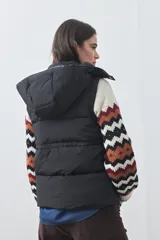 Chaleco puffer negro con diseño acolchado, capucha desmontable y cierre frontal. Cuenta con cordones ajustables en la cintura y bolsillos laterales.