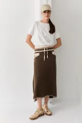 Falda midi de lana en color marrón, con diseño acampanado y tejido acanalado. Presenta una cintura elástica con cordón de ajuste, detalles de rayas en tonos beige y blanco en la parte superior, y costuras decorativas en el ruedo.