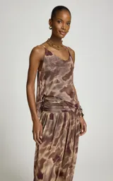 Blusa de tul sin mangas, con escote en V, tirantes finos y estampado orgánico en tonos marrón y beige. Presenta diseño fluido, suave transparencia, bajo asimétrico con puntas alargadas y corte recto.