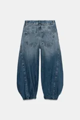 Jeans de tiro medio confeccionados en denim azul con efecto deslavado, corte holgado con diseño de volumen abullonado en las piernas y bajo con puño elástico. Cuentan con trabillas, bolsillos delanteros y traseros, y costuras decorativas marcadas.