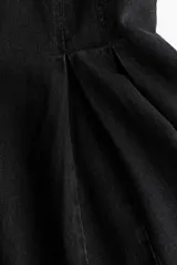 Vestido corto sin mangas en denim negro, con escote redondo, cuerpo entallado y falda acampanada con pliegues.