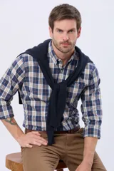 Camisa de manga larga con estampado de cuadros en tonos azul, beige y naranja. Presenta cuello abotonado, cierre frontal con botones y un bolsillo pequeño en el pecho.