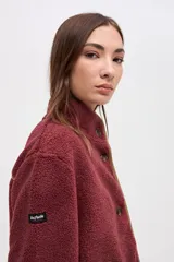 Campera de sherpa doble faz color bordó, con cierre frontal de botones, cuello alto y bolsillos laterales. Presenta detalles de vivos en nylon color tostado en los bordes y costuras.