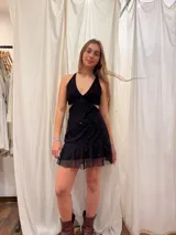 Vestido corto plateado con lentejuelas, escote en V y cut-outs laterales bajo el busto. Breteles finos que se cruzan en la espalda y atan atrás. Volado en el ruedo.