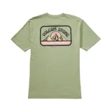 Remera verde claro de manga corta, con cuello redondo y un bolsillo en el pecho que incluye un pequeño estampado gráfico con el texto 'Volcom Stone' y diseño de montañas.