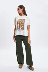 Remera de manga corta color crudo con estampa frontal rectangular en tonos marrones y dorados con diseño floral y la frase 'Grow as you go'.