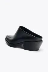Zueco de piel color negro con diseño estilo biker. Presenta una correa decorativa con tachas metálicas y una anilla extraíble en el lateral. Cuenta con punta cuadrada y tacón bajo.