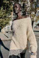 Jersey de punto con cuello barco y manga larga, confeccionado en tejido efecto cepillado. Presenta un diseño asimétrico en el bajo con detalle de encaje aplicado.