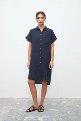 Vestido camisero azul marino de lino, corte recto, largo a la rodilla, con cuello clásico, manga corta y abotonadura frontal.