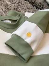 Buzo de corte oversize con diseño de rayas horizontales anchas en color verde y crudo. Presenta cuello redondo, mangas largas y puños elásticos, confeccionado en tela con interior de felpa.