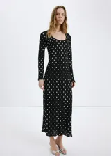 Vestido largo negro con estampado de lunares blancos, de corte recto, escote redondo y mangas largas.