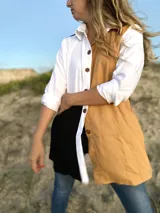 Camisa larga de lino con diseño color block en blanco, negro y ocre. Tiene cuello clásico, mangas largas con puños abotonados y cierre frontal con botones de madera.