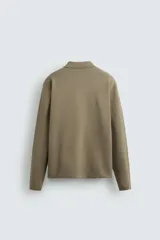 Polo de punto de manga larga con cuello solapa y cierre frontal de botones. Presenta un diseño de corte regular con aberturas laterales en el bajo.